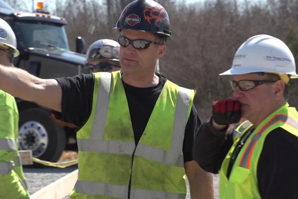Two men in safety vests and hardhats working together